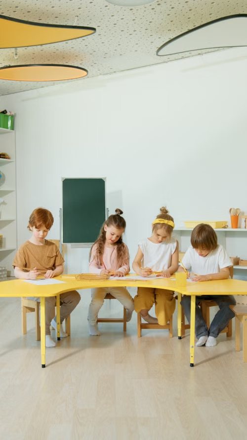 Cuatro niños haciendo ejercicios en una mesa amarilla del aula
